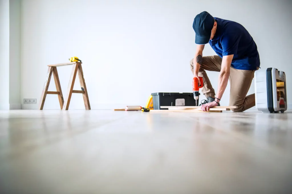 Pessoa realizando manutenção no piso de um apartamento, com ferramentas ao redor, dentro de uma obra residencial, relacionado às leis do condomínio.
