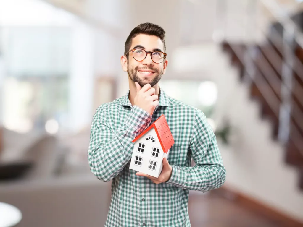 Homem sorridente segurando uma maquete de casa, simbolizando a alienação fiduciária de imóvel, conceito importante nas operações de financiamento imobiliário.